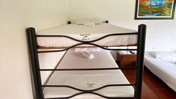 Een stapelbed met een witte matras, gelabeld 'Privado Cocote', en een enkel bed met een witte matras in een kamer met houten balken in het plafond en een schilderij aan de muur.