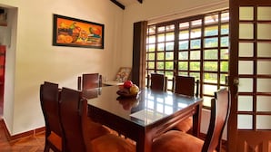 A dining area with a wooden table and chairs, a painting on the wall, and a window with a view of greenery. - Paraiso Cocora (Salento)