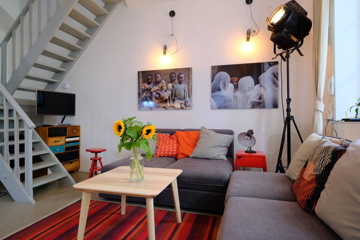 A living room with a staircase, a sofa, a coffee table with a vase of sunflowers, and a TV.