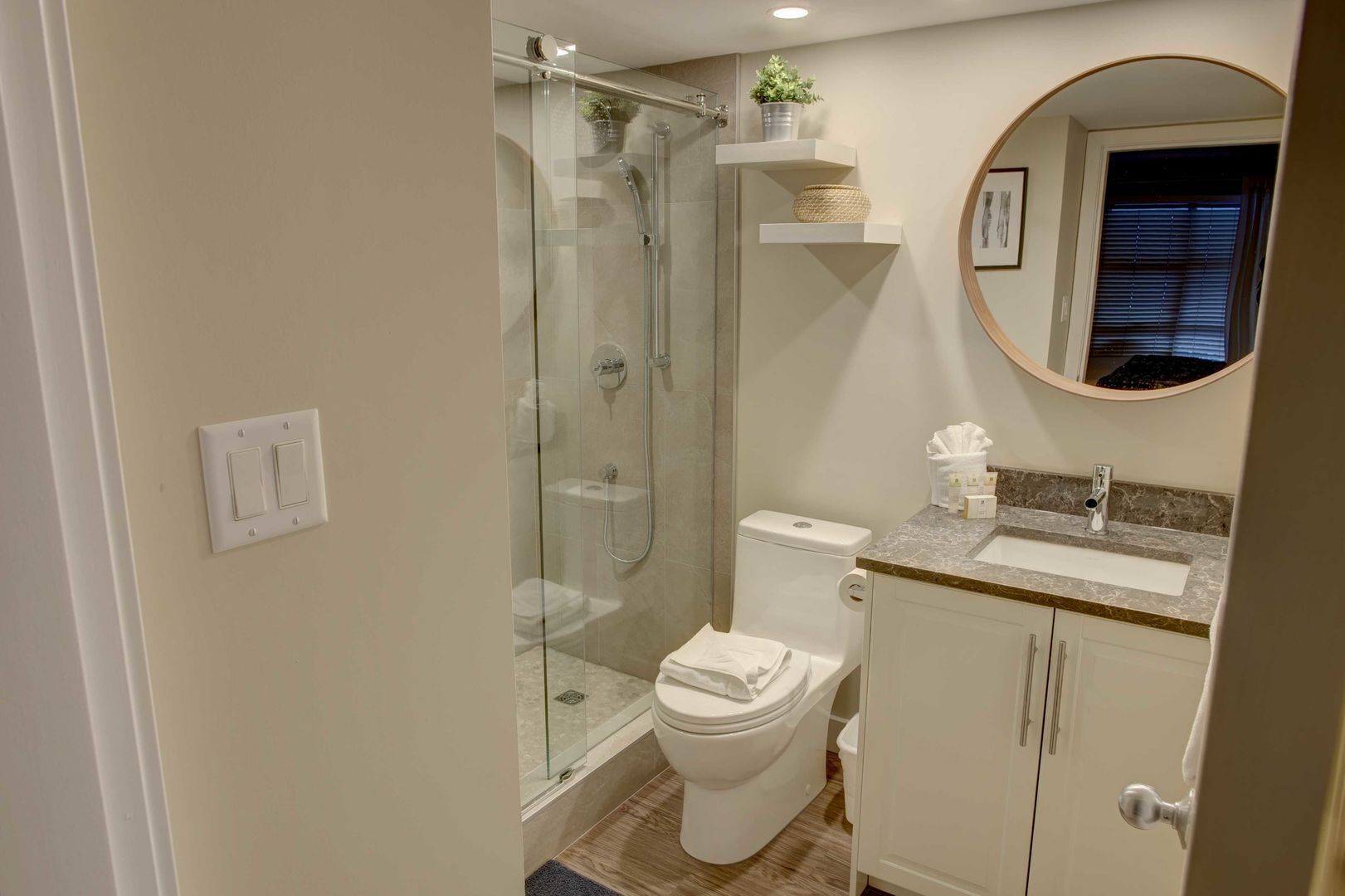 A modern bathroom with a glass-enclosed shower, a toilet, a sink with a marble countertop, and a mirror above the sink.