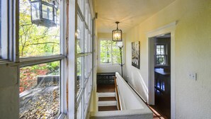 A hallway with a staircase, a hanging light fixture, and a view of trees through large windows. - Top-Floor Princeton Condo w/private balcony (Princeton)
