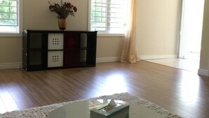 A spacious room with a large window, a clock on the wall, and a round glass table with a tissue box. - Walkout Ravine, Cottage feeling basement (Richmond Hill)
