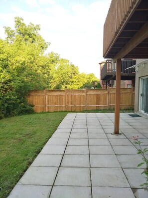 Enjoy a serene outdoor space with a paved patio, wooden fence, and pergola, surrounded by a lush lawn and trees.