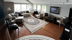 A modern living room with a large window, a flat-screen TV, and a patterned rug. - Lake Muskoka in Muskoka Bay (Gravenhurst)