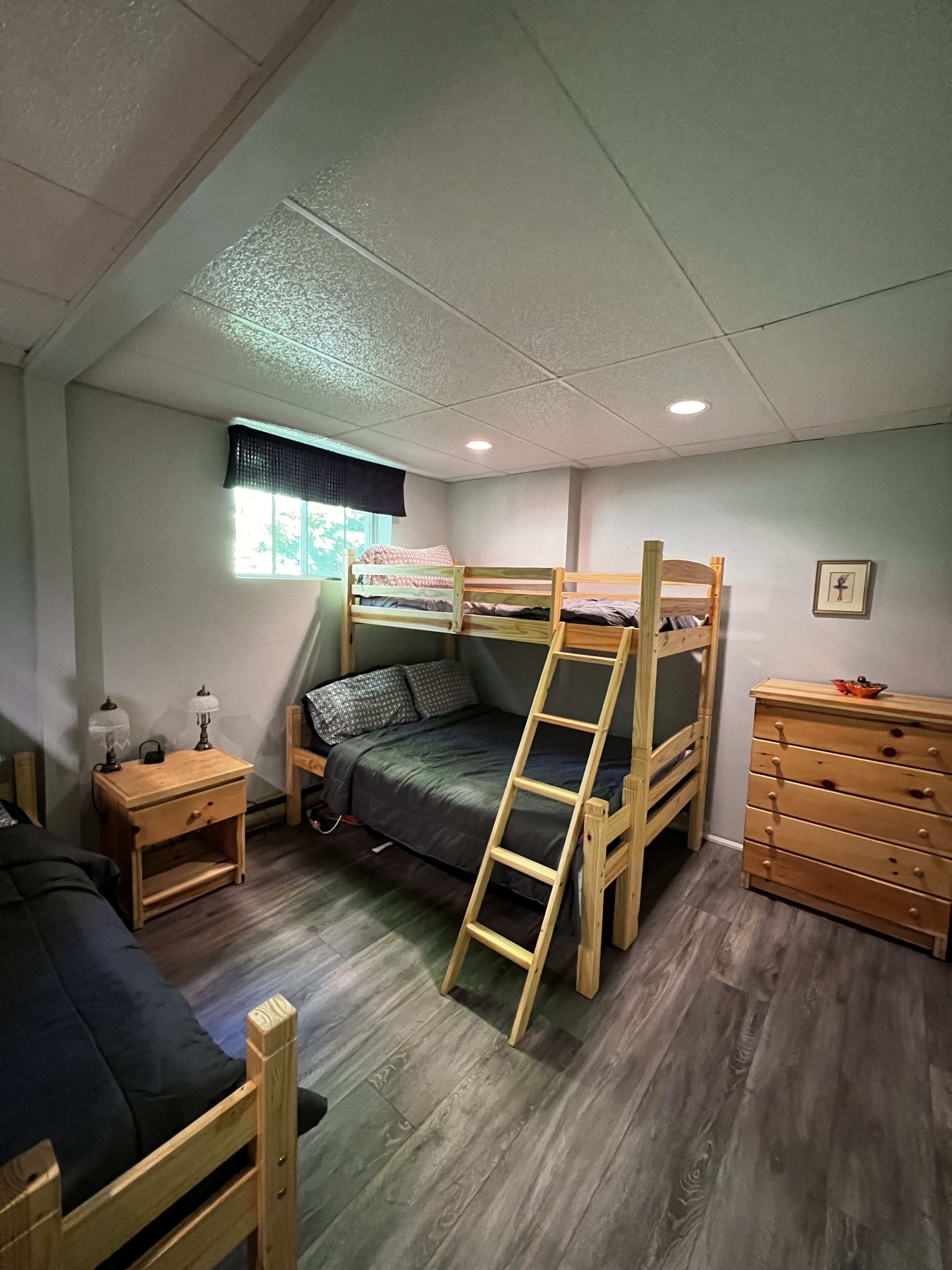 A bunk bed room with a wooden ladder, a nightstand with a lamp, and a dresser.