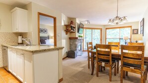 A kitchen with a granite countertop, white cabinets, and a dining area with wooden chairs and a table. - Aspens #444 Prime Ski-in Ski-out Location! Pool, Hot tubs, BBQ, sleeps 6 (Whistler)