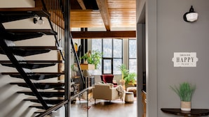 A modern interior with a wooden staircase, a red chair, and a sign stating "THIS IS OUR HAPPY PLACE." - Lamplighter Grand Loft - contemporary open design & walk anywhere! (Nelson)