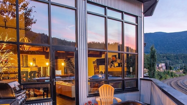 A wooden deck with a hot tub, a glass-enclosed patio area, and a view of a mountainous landscape. - Lamplighter Grand Loft - contemporary open design & walk anywhere! (Nelson)