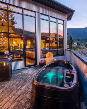 Un patio di legno con idromassaggio, un'area patio in vetro e vista su un paesaggio montuoso.