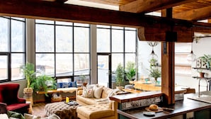 A spacious living room with a large window, a red chair, a beige sofa, and a kitchen area with a sink and countertop. - Lamplighter Grand Loft - contemporary open design & walk anywhere! (Nelson)