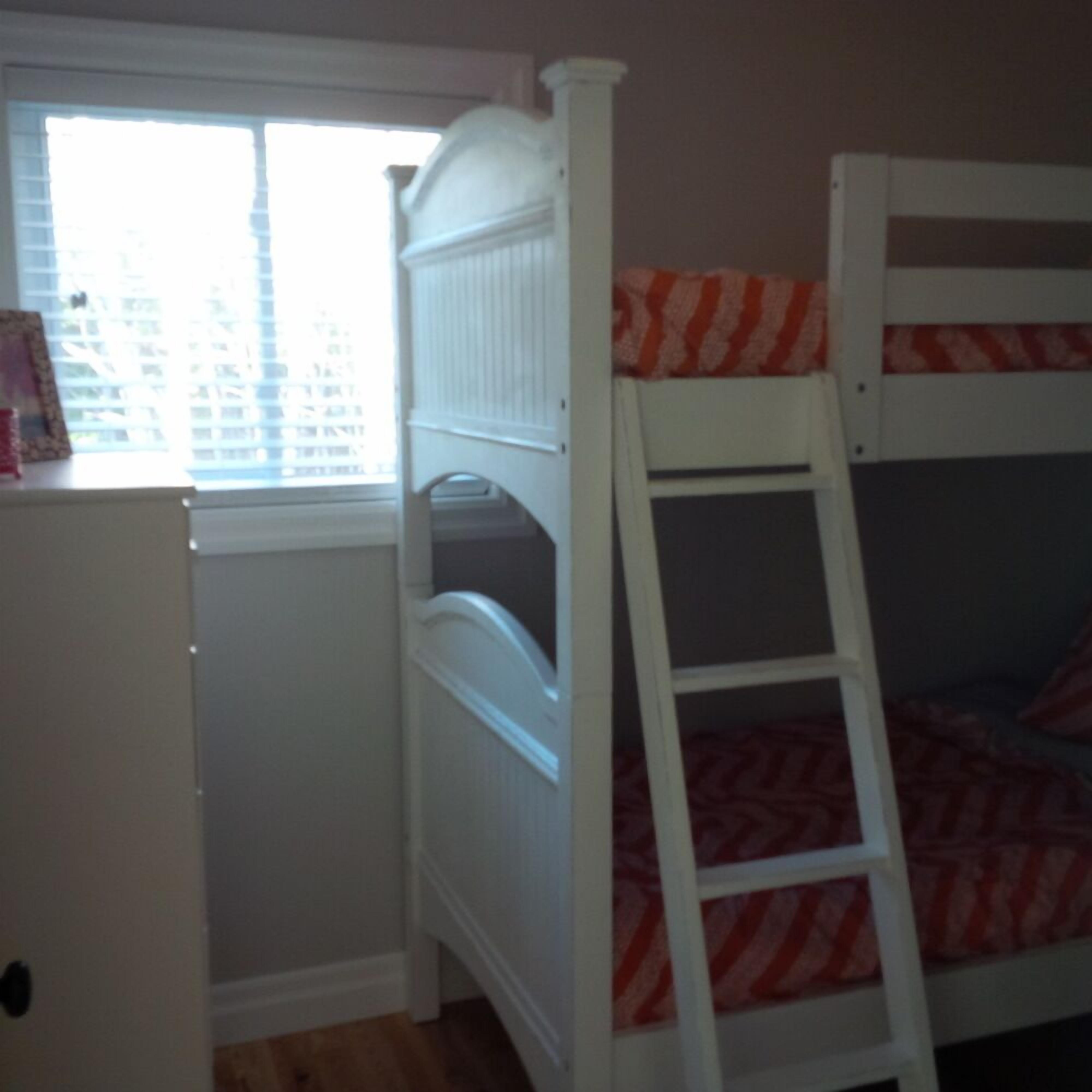 A bunk bed with a ladder, a white dresser, and a window with blinds.