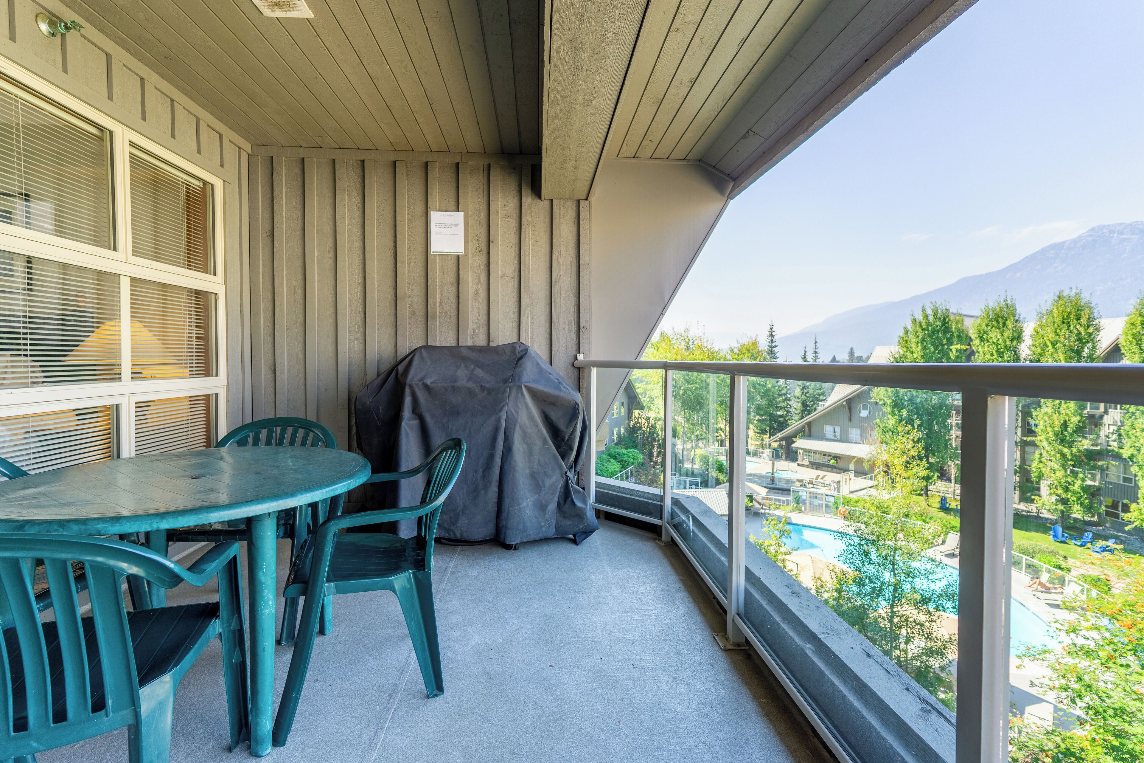 Un balcon avec une table et des chaises, un barbecue et une vue sur une piscine et des bâtiments en arrière-plan.