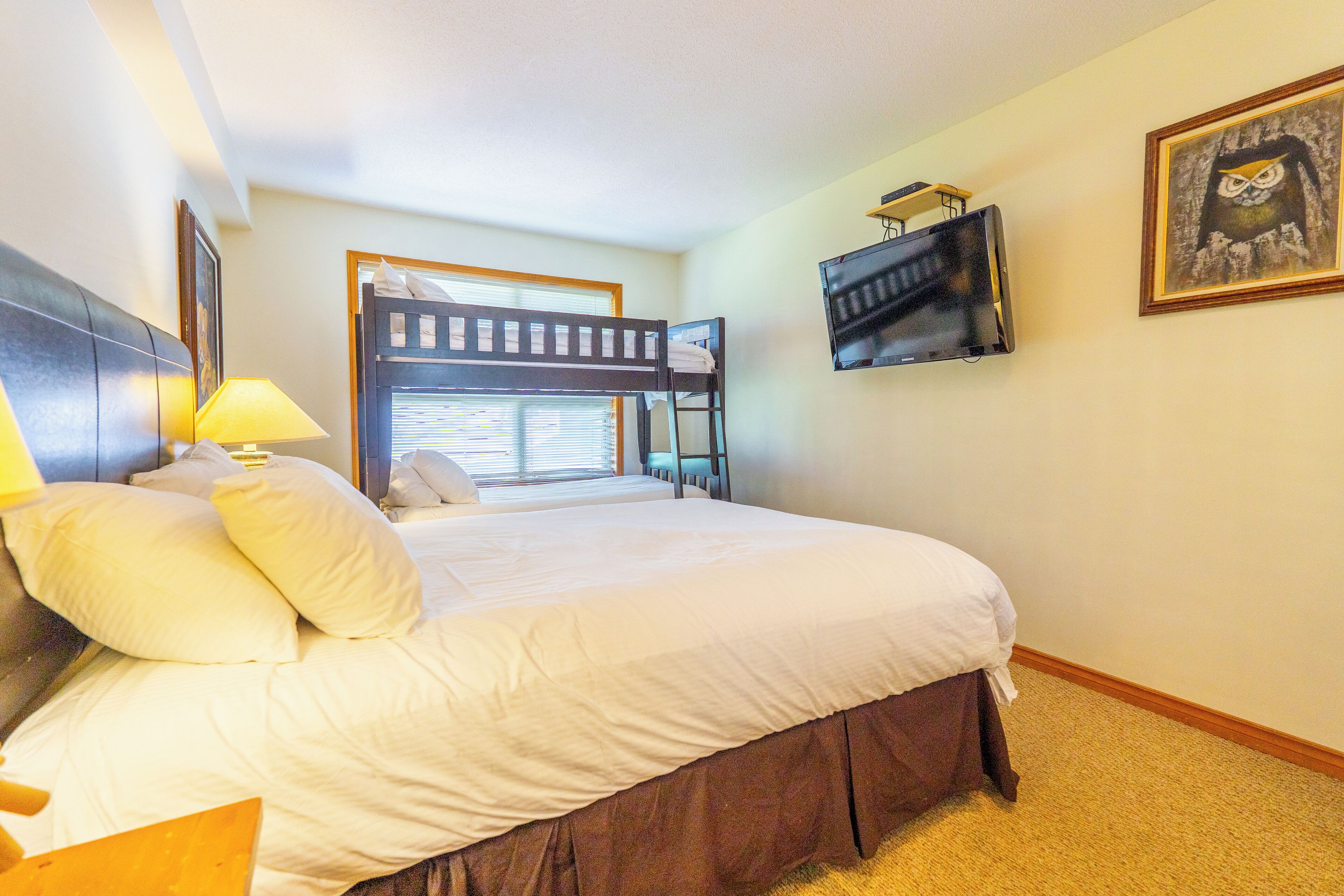 A hotel room with a large bed, a TV mounted on the wall, and a window with blinds.