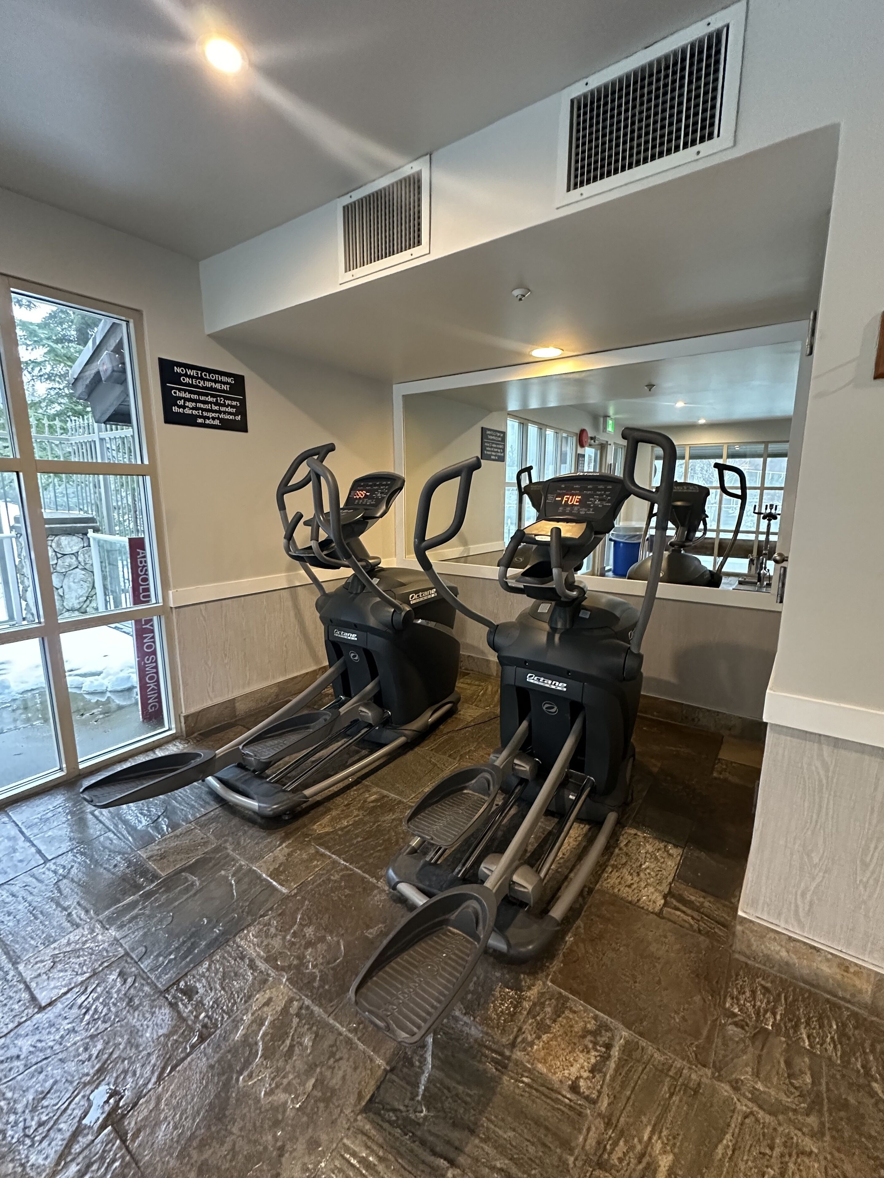 Une salle de sport équipée de tapis de course, de vélos d’appartement et d’un mur recouvert de miroirs.