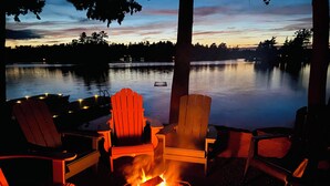 A lakeside seating area with Adirondack chairs and a fire pit. - Family Friendly Stoney Lake Cottage (Lakefield)