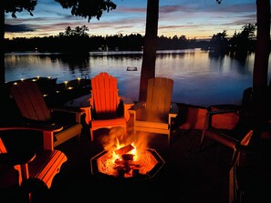 A lakeside seating area with Adirondack chairs and a fire pit.