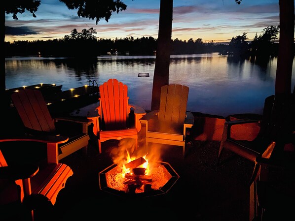 Un espace aménagé au bord du lac, avec des fauteuils Adirondack et un foyer.