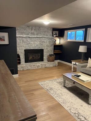 Un salon avec une cheminée en pierre, un plancher en bois, un canapé, une table basse et une lampe.