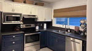 A modern kitchen with white cabinets, stainless steel appliances, a window with a view, and a ceiling light fixture. - Family Friendly Stoney Lake Cottage (Lakefield)