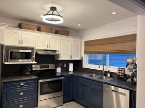 A modern kitchen with white cabinets, stainless steel appliances, a window with a view, and a ceiling light fixture. - Family Friendly Stoney Lake Cottage (Lakefield)