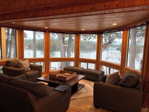 Un intérieur de chalet chaleureux, doté de grandes fenêtres, d’une cheminée et d’un coin salon confortable.