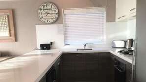 A modern kitchen with a large island, dark cabinetry, a clock, and a window with blinds.