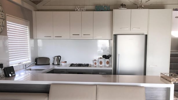 A modern kitchen with white cabinets, a stainless steel refrigerator, and a built-in island with a sink.