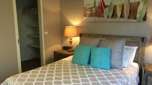 A bedroom with a bed, a nightstand, a lamp, a painting, and a closet.