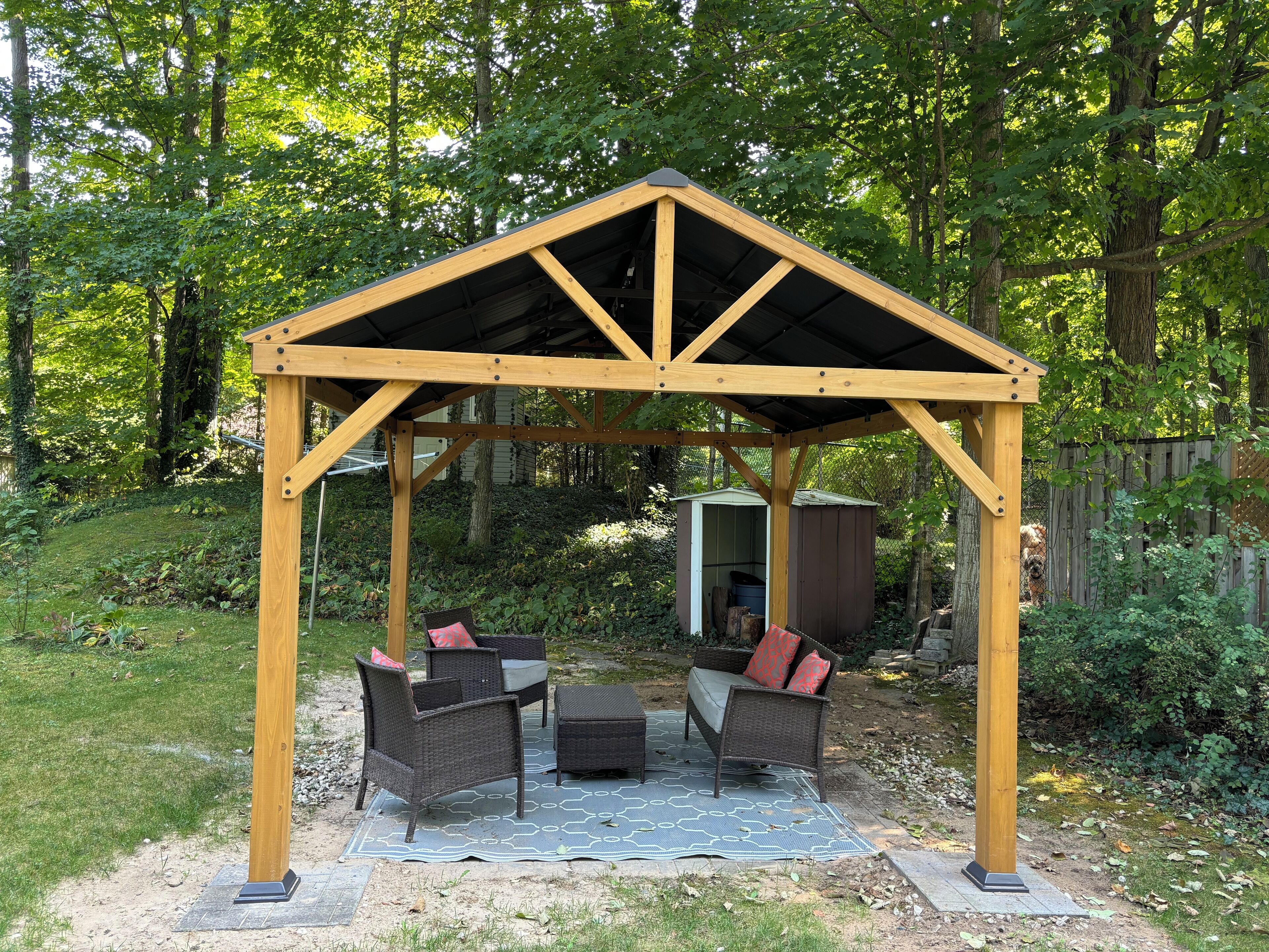 A wooden gazebo with a triangular roof and a table and chairs underneath.