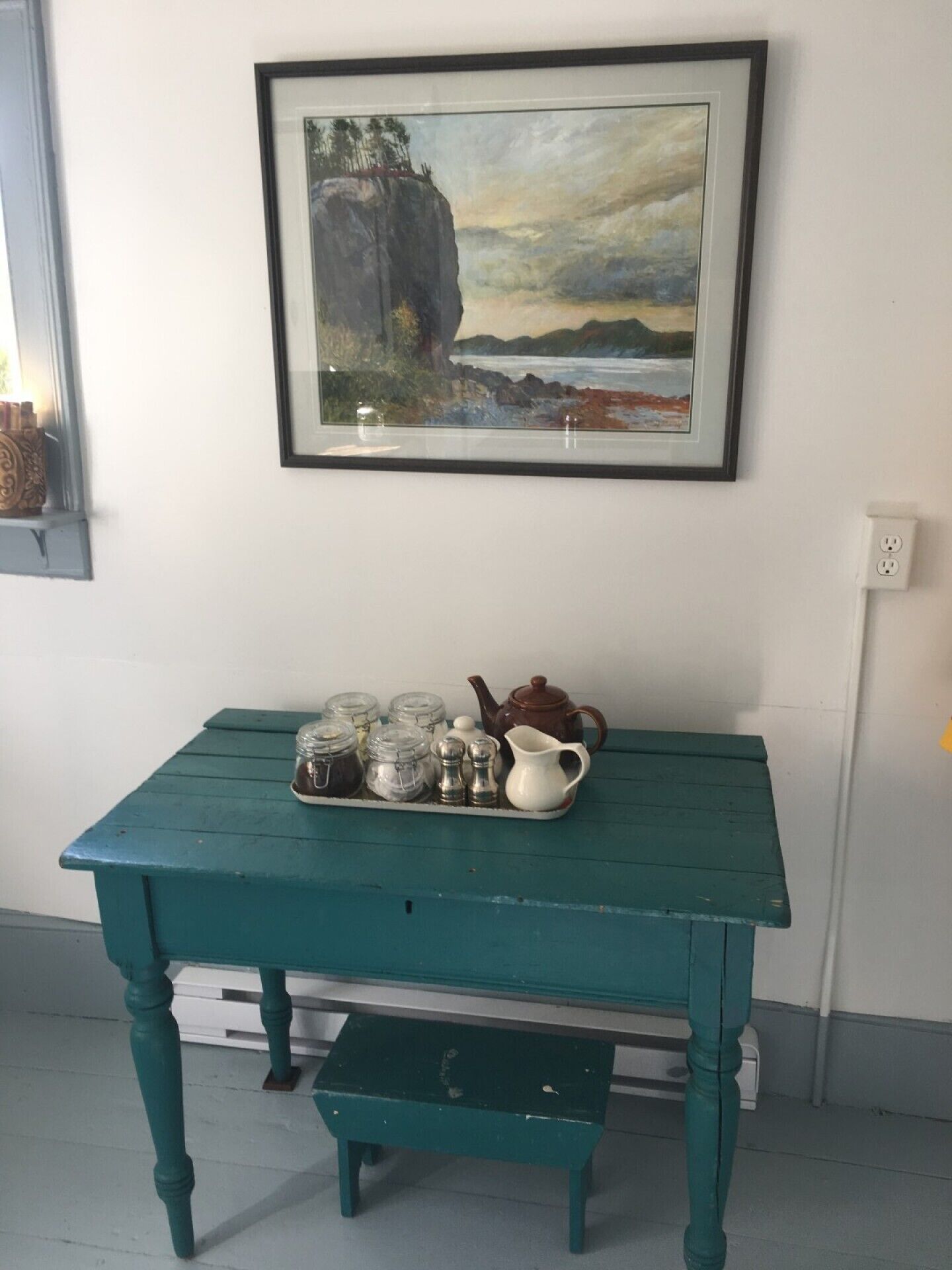 Una mesa de madera azul verdoso con una bandeja que contiene frascos, una jarrón y una tetera.