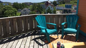 Une terrasse en bois avec deux fauteuils Adirondack turquoise et une nappe à motifs.