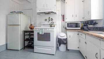 Een kleine keuken met witte kastjes, een kookplaat, een magnetron en een koelkast.