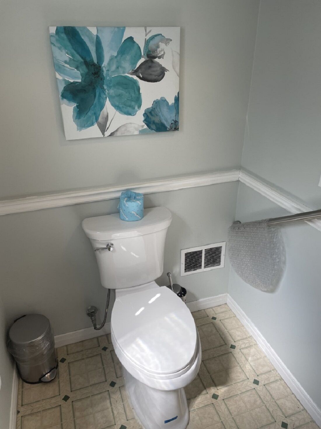 A bathroom with a toilet, a trash can, and a vent.