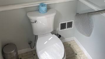 A bathroom with a toilet, a trash can, and a vent.