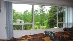 A room with large windows, a patterned sofa, and a view of a house and trees. - Simcoe Georgina Family Cottage Winter-Summer Rent 1hr from Toronto (Willow Beach)
