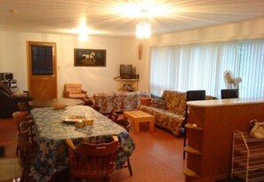 A living room with a dining table, sofas, a TV, and a fan.