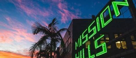 A building with a neon sign reading "MISSION HILLS" against a twilight sky.