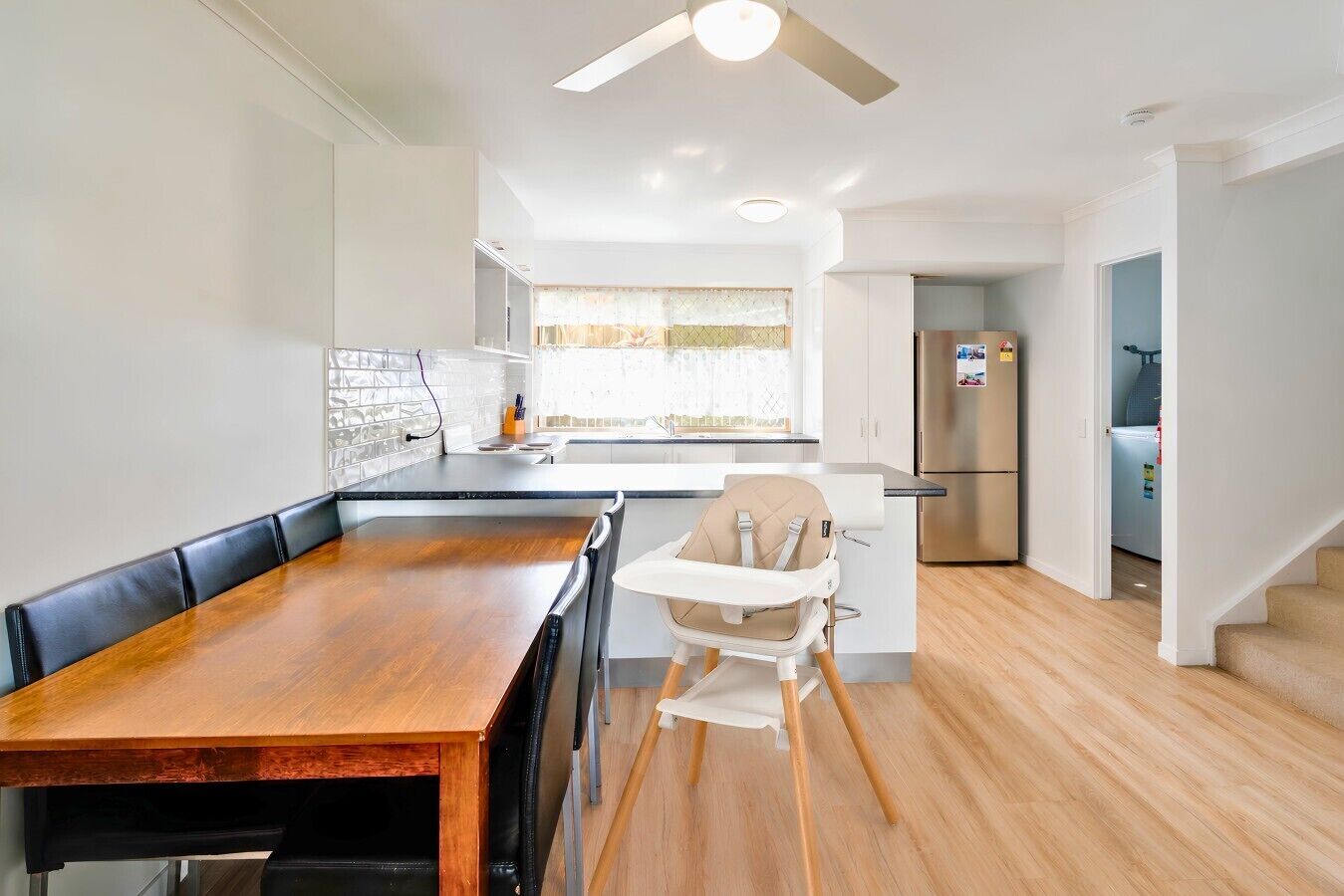 A modern kitchen with a dining table, a high chair, and a refrigerator.