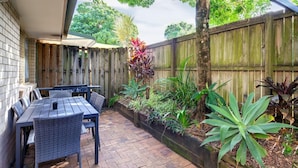 Une terrasse avec une table et des chaises, entourée d’une clôture en bois et agrémentée de différentes plantes.