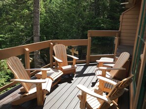Relax in style with Adirondack chairs and a small table on this deck, surrounded by a forest view.