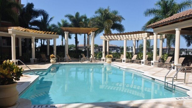 A pool area with lounge chairs and umbrellas, surrounded by palm trees.