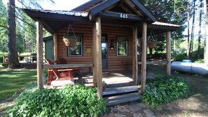 A rustic cabin with a porch, numbered 805, surrounded by greenery.