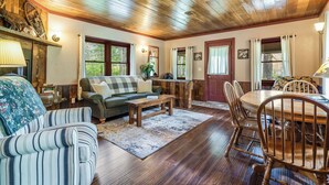 A cozy living room with wooden flooring, a sofa, a coffee table, and a dining table with chairs.