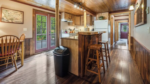 A rustic kitchen with wooden cabinets, a bar area, and a dining space with wooden chairs.