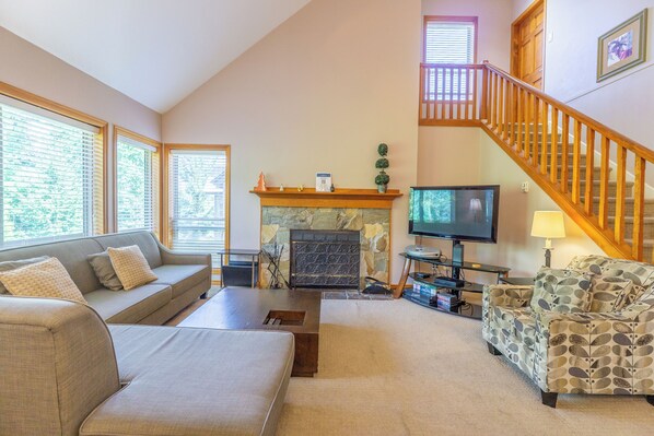 A living room with a fireplace, a television, a sofa, a coffee table, and a patterned armchair. - Painted Cliff 16 Ski-in, Ski-out Luxury with serene mountain views, sleeps 8 (Whistler)