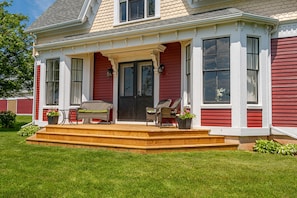 A house with a red exterior, a front porch with wicker furniture, and a well-maintained lawn. - Wexford Heritage House - Cumberland, Prince Edward Island (Cumberland)