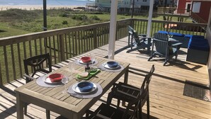 Eine Holzdar Terrasse mit Esstisch, mit Blick auf einen Strand.