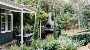 A patio area with a stone pizza oven, outdoor seating, and lush greenery.