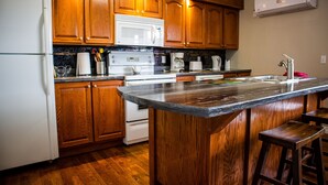 Une cuisine avec des meubles en bois, un réfrigérateur blanc, un four à micro-ondes, une cuisinière et un grand îlot central avec des tabourets.