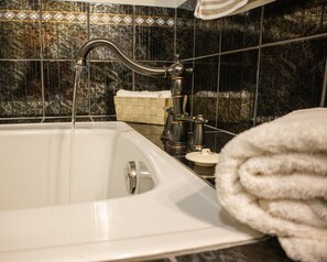 A bathtub with running water, a towel, and a basket on the counter. - Peridot By The Shore,  Rocky Harbour Newfoundland (Rocky Harbour)